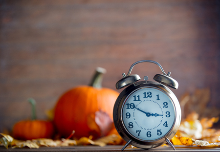 Vintage alarm clock and maple tree leaves with pumpkins on yellow wooden background with bokeh.の写真素材