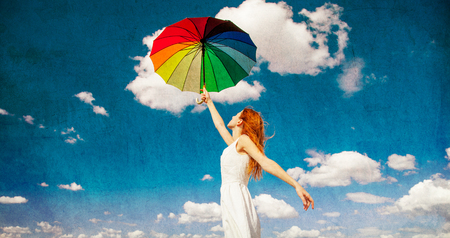 Redhead girl holding umbrella at autumn cloudscape background. Outdoor imageの写真素材