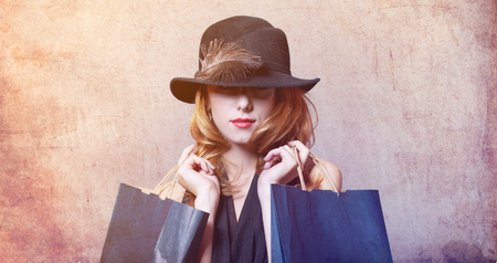 Style redhead woman in hat with feather holding shopping bags on grey backgroundの写真素材