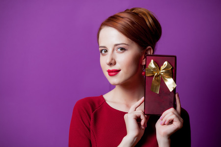 Portrait of young redhead woman with gift box on purple backgroundの写真素材