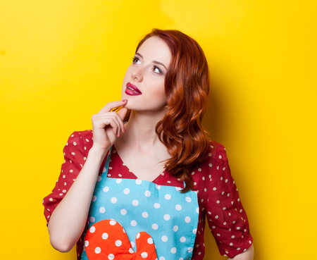 Young redhead housewife with gloves on yellow backgroundの写真素材