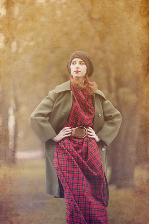 Young redhead woman in red dress with green coat at autumn outdoorの写真素材