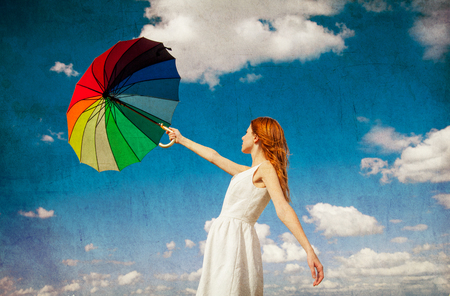 Redhead girl holding umbrella at autumn cloudscape background. Outdoor imageの写真素材