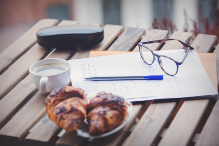 balance on a paper at breakfast time. On a table are cloissant and cup of coffee