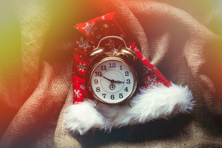Christmas Santa Claus hat and vintage alarm clock on jute backgroundの写真素材