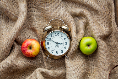 Apples and alarm clock on jute sack background. Autumn season harvestの写真素材