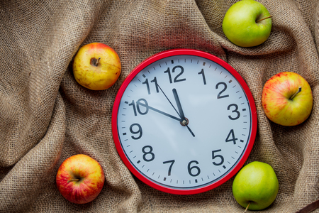 Apples and alarm clock on jute sack background. Autumn season harvestの写真素材
