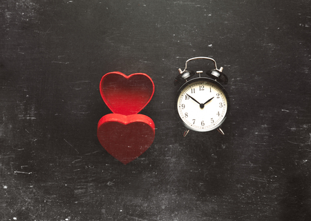 Heart shape box and black vintage alarm clock on grey background with scratches の写真素材