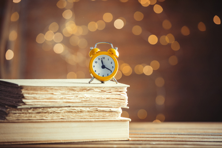 vintage alarm clock and old books on wooden table at fairy lights background. Libraryの写真素材