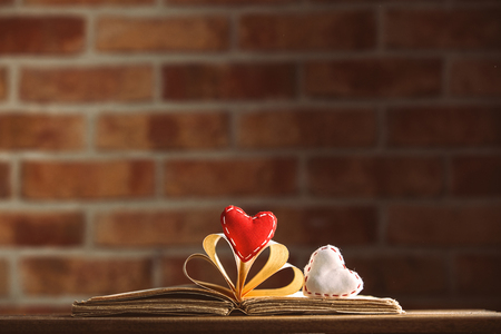 Heart shapes and old book on wooden table at brick wall background. Libraryの写真素材