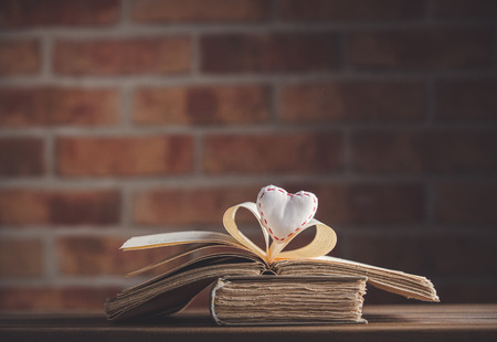 Heart shape and old book on wooden table at brick wall background. Libraryの写真素材