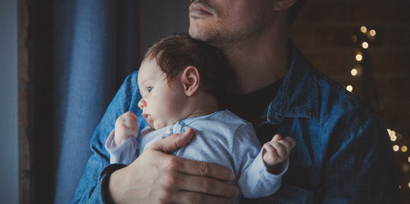 Photo of little infant in father's hands near a window. Image made with natural day light.の写真素材