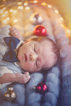 Funny little baby wearing a costume lying down on knitted plaid.  Infant just borned, have a one week. Fairy or Christmas lights on background. の写真素材