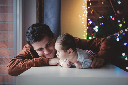 Young father help to a little child lie down on tummy in first time. Indoor image with focus on...