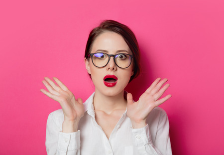 Portrait of young surprised businesswoman in eyeglasses on pink background. の写真素材