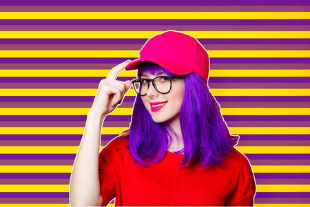 Woman with purple hair and eyeglasses in hat at striped backgroundの写真素材