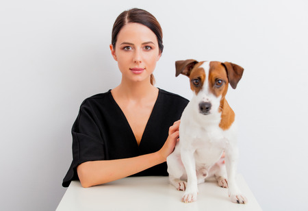 Pretty redhead caucasian woman in black dress with dog sitting at white table in lagom style on white backgroundの写真素材