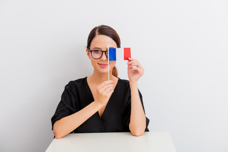 Pretty redhead caucasian woman in black dress with french flag sitting at white table in lagom style on white backgroundの写真素材