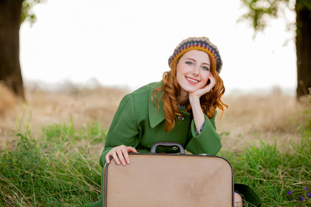 portrait of adult girl in green coat with suitcase sitting at grass at countryside outdoor.の写真素材