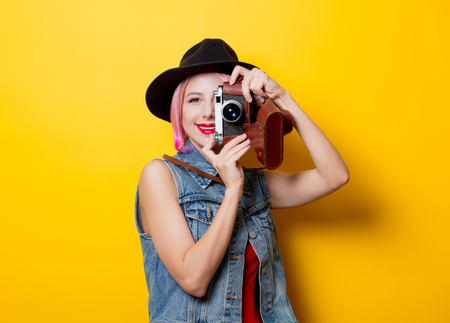 Portrait of young style hipster girl with pink hairstyle with retro camera on yellow backgroundの写真素材