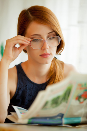 Young girl reading newspaper in eyeglasses at homeの写真素材