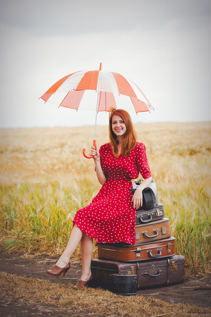 Young redhead girl with umbrella and bags travel around the world. Outdoor at countryside の写真素材