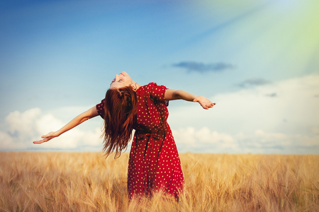 Young redhead girl with open hands standing at wheat field in summer timeの写真素材