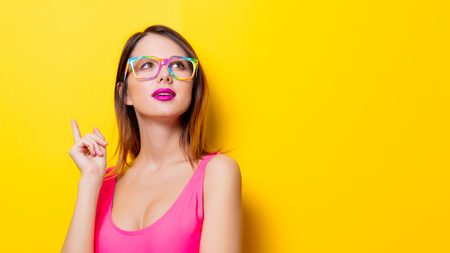 Young girl in pink one-piece swimming suit with eyeglasses on yellow backgroundの写真素材