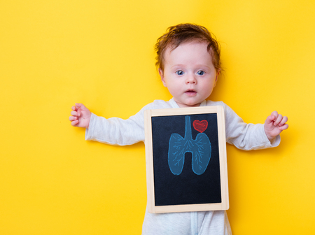 little baby with X-ray board and drawing lungs and heart on yellow background