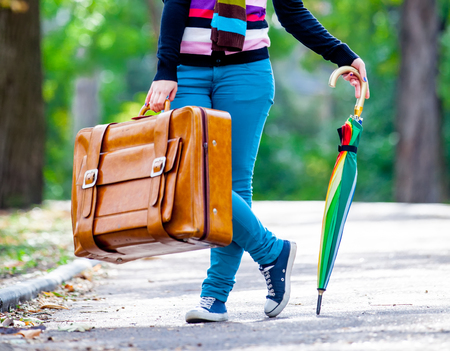 Young teen girt with suitcase and umbrella in a park in sunny dayの写真素材