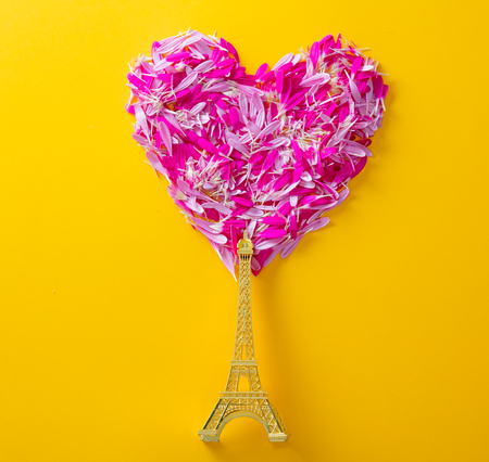 Pink and purple flower petals in heart shape and golden Eiffel tower statue souvenir on yellow background.の写真素材