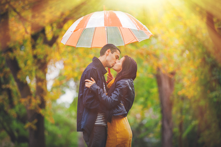Young couple in love kissing under umbrella at autumn season outdoorの写真素材