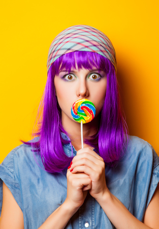 Young girl with purple hair and lollipop on yellow backgroundの写真素材