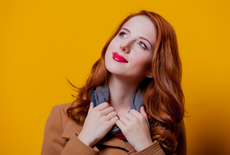 Young redhead girl in coat on yellow background の写真素材