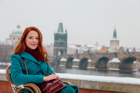 Young redhead girl sitting in chair with Old Town Prague city on background in winter time. Czech Republic の写真素材
