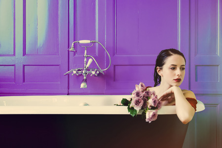 portrait of beautiful young woman sitting in bath holding bunch of roses and relaxingの写真素材