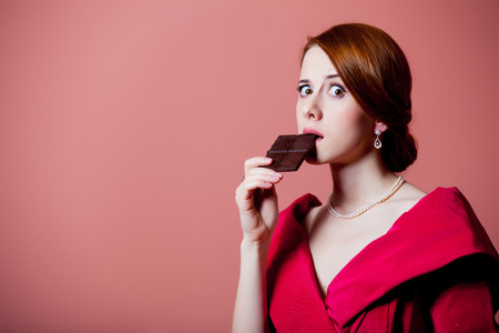 Young surprised woman in red Victorian epoch clothes with chocolate on pink backgroundの写真素材