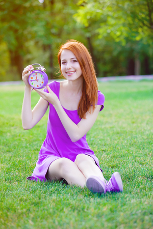 Redhead girl with litle alarm clock in summertime park outdoor