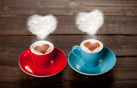 Two color cups of coffee with heart shape steams on wooden tableの写真素材