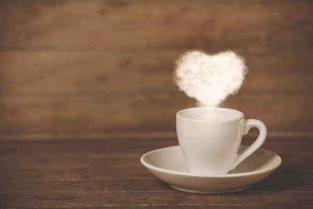Cup of coffee with ehart shape steam on a tableの写真素材