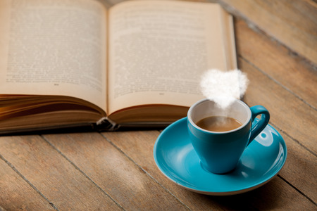 Cup of coffee with heart shape steam and open book on wooden tableの写真素材