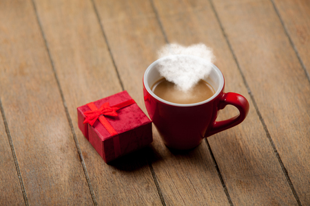Red cup of coffee with heart shape steam and gift box on wooden backgroundの写真素材