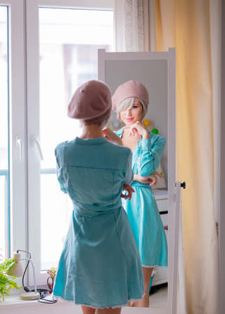 Young girl in beret with short hairs dressing up near mirror at home.の写真素材