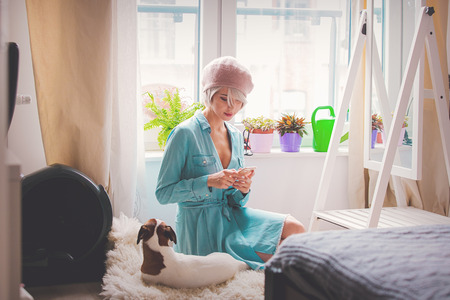 Young girl with pink hair and beret with dog typing with mobile phone at home.の写真素材