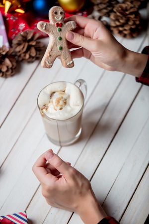 Female hands gingerbread man cookie and cup of coffee on a wooden table with gifts aroundの写真素材