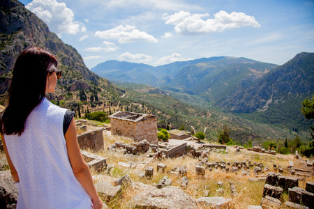 Young girl in white clothes standing on rock in Greece with view at mountains