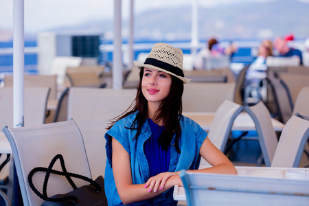 Happy redhead girl in blue dress and hat have a voyage on a boat in Greece.の写真素材