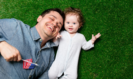 Father and son lying down on green grass with USA flag.