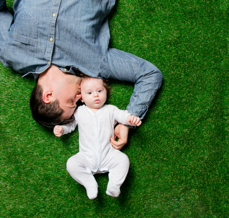 Young father and son lying down on green grass. Above view