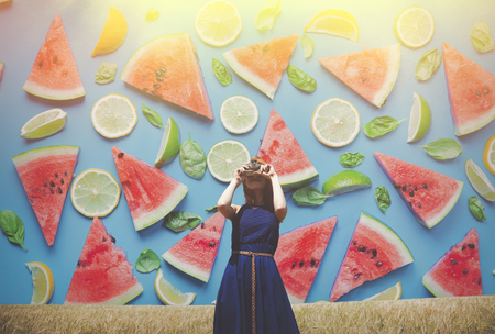 Redhead girl at spring field with retro camera with watermelon and lime on backgroundの写真素材